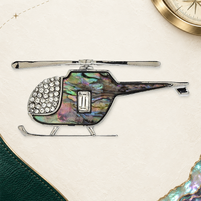Abalone-Look Helicopter Brooch on an elegant ivory, evergreen and gold travel-inspired background